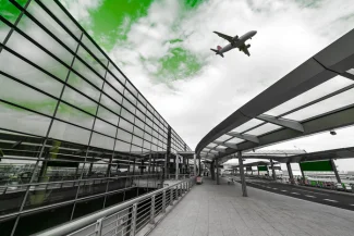 Perspective shot of a modern airport terminal facade with a sleek walkway leading up to the building, as a plane takes off overhead. The sky is tinted green, representing the Dubai Airport Free Zone (DAFZA).