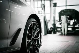 Close-up, black and white photograph of the tire and fender of a luxury car inside a bright service or maintenance bay, symbolizing the Dubai Auto Zone and automotive industry.