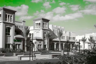 Low-angle view of the distinct, low-rise architecture of Dubai Knowledge Village, featuring traditional Gulf-style buildings, palm trees, and an intense green sky.