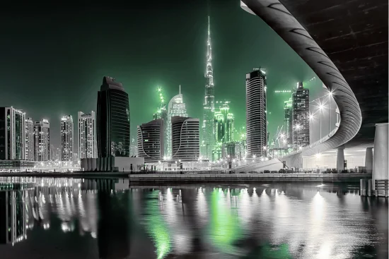Night view of a modern skyline featuring the Burj Khalifa and surrounding skyscrapers reflected in the water, with construction cranes and lights prominently colored bright green. This visual represents the benefits and opportunity of Sharjah Mainland business setup.