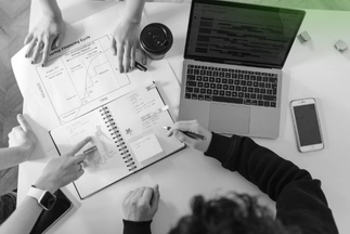 Top-down view of a business team collaborating, pointing at a printed graph and writing notes in a planner next to a laptop during a strategic meeting.