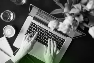 Overhead shot of a person's hands typing on a laptop, representing content creation or digital work.