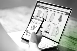 Mobile e-commerce or online shopping, showing a phone with a cart icon over a laptop displaying clothes.