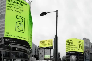 Large, neon green digital billboards in a city square displaying public health messages (like "Stop the spread of COVID-19"), symbolizing large-scale outdoor or online display advertising.