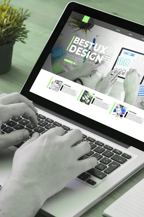 Close-up of hands typing on a laptop with the screen displaying "BEST UX DESIGN" and web design elements.