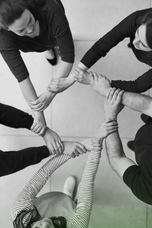 Overhead view of a diverse group of people interlocking arms in a circle, symbolizing teamwork, collaboration, and a unified work process.