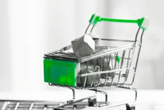 A close-up of a miniature metal shopping cart with green handles and a green front panel, filled with small grey packages, symbolizing e-commerce and Google Shopping Ads.