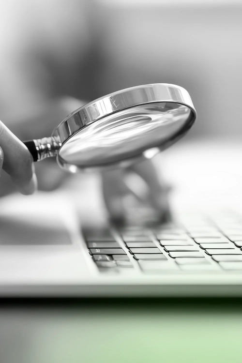 A magnifying glass held over a laptop keyboard, symbolizing research, analysis, or the search process in SEO.